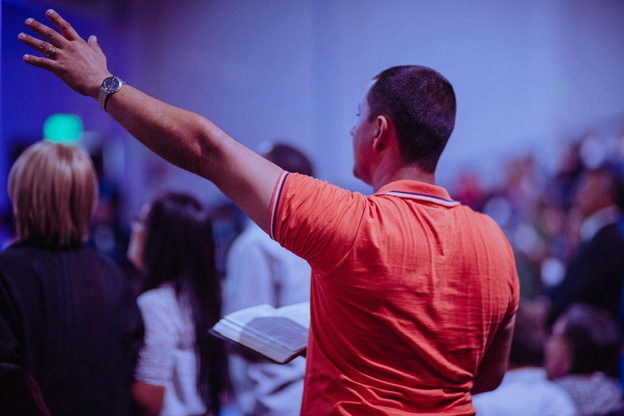 A person stands in a crowd raising a hand, conveying a tone of worship and engagement.