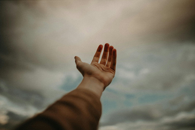 A hand reaching towards a cloudy sky, evoking hope, trust, and faith.