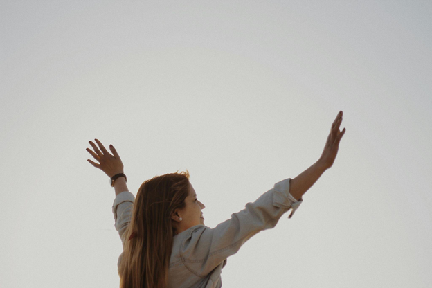 Woman with outstretched arms against a clear sky, conveying hope and joy.