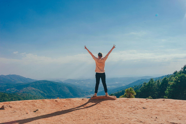 A person stands on a cliff edge with arms raised in a victory pose.