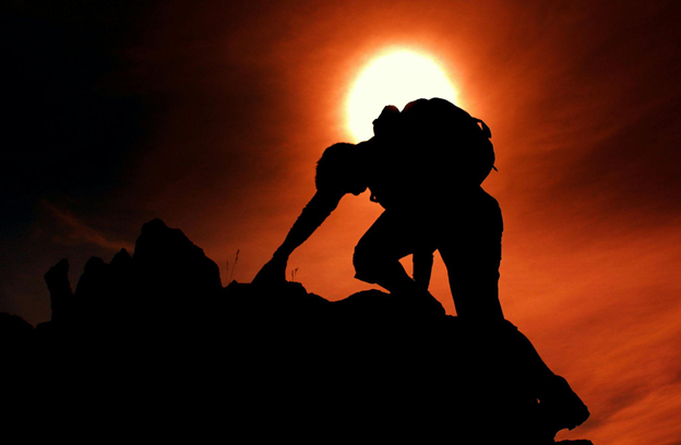 Silhouette of a climber ascending rocky terrain with a glowing sun in the background.