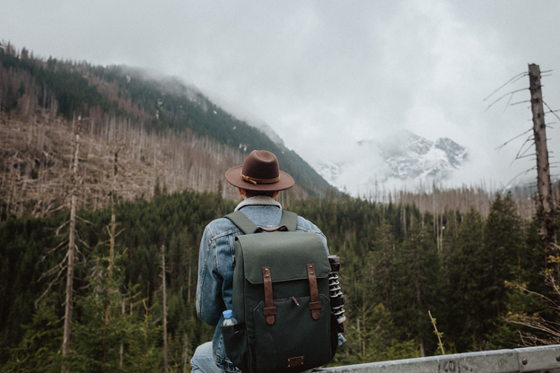 A man rests on a bench with a backpack, overlooking a mountain view, symbolizing the journey of pioneer families.
